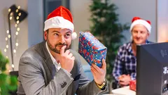 Man in Santa hat holding Christmas gift looking at computer screen during virtual celebration