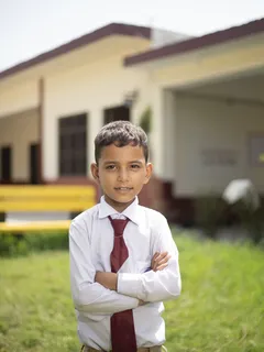 Young boy in school uniform with tie standing outside building in Pakistan