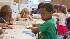 Young African-American boy in green sweater drawing on white paper in Atlanta school