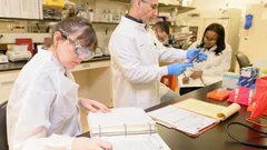 Scientists in lab coats conducting research and recording data in a laboratory