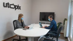 Two professionals wearing masks working on laptops in office meeting room