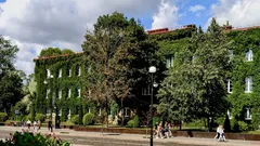 Building covered in green ivy surrounded by trees and people walking on sidewalk