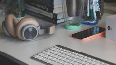 grey and white keyboard next to grey headphones on desk with pink teal accents