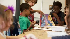 Four boys at school table drawing with crayons from cartoon book in Atlanta primary class