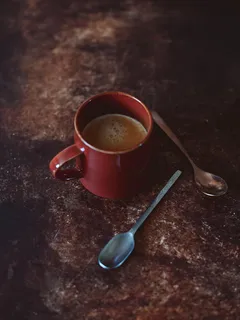 Red ceramic mug with stainless steel spoon inside on white background
